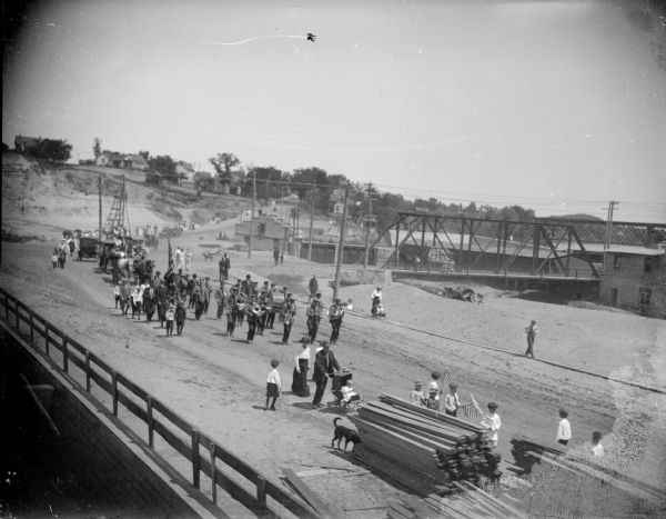 Elevated view of spectators and a marching band leaving a parade. There are bridges crossing a river in the background.