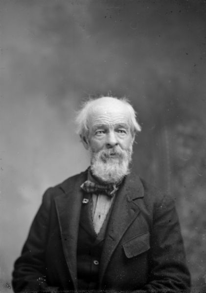 Waist-up studio portrait of an elderly European American man, partially bald, sitting and wearing a dark-colored suit coat, vest, and bow tie. Man identified as the father of Ed Lyon.