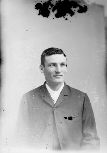 Waist-up studio portrait of a European American man posed sitting and wearing a dark-colored suit coat, vest, and light-colored necktie.