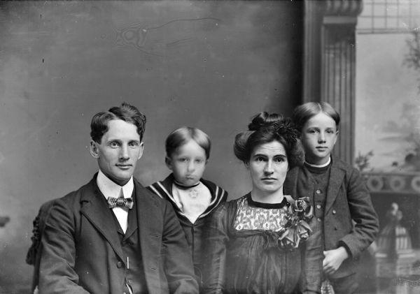 Waist-up studio portrait in front of a painted backdrop of an unidentified man and woman posing sitting with two boys posing standing behind them.