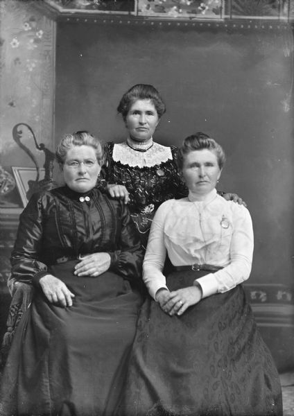 Group portrait of unidentified group of women. Two women are sitting on the left and right, with a woman standing behind them.