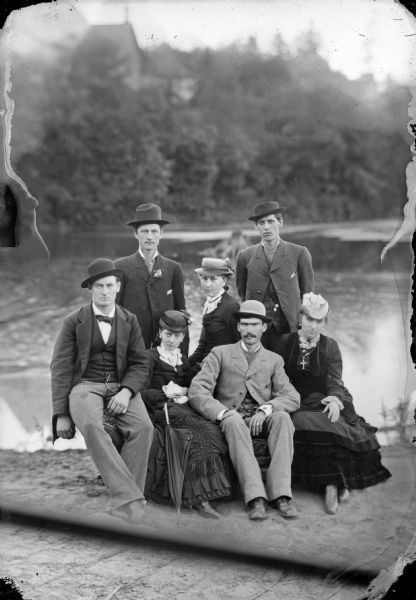 Exterior portrait next to a river of two men and three women posing sitting, and two men posing standing behind them.