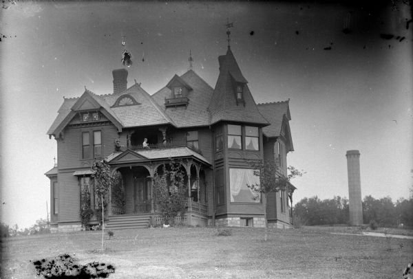 Exterior view of the home of W.R. O'Hearn in Black River Falls, near 9th Court, just south of the water standpipe in the background. Three children are posing on the balcony above the front porch.