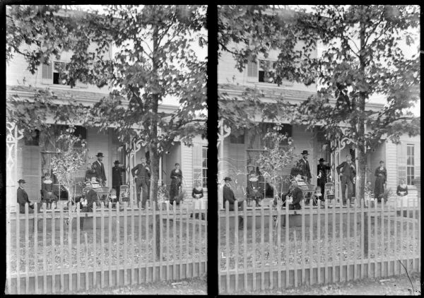 Stereograph of people posing on the porch and yard of a wooden house. Identified as the home of J.J. McGillivray, located on the east side on the northwest corner of Main and 8th Streets.
