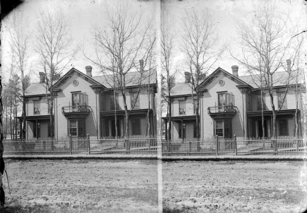 View from street, in a stereograph form, of a two-story wooden house, identified as the northwest corner of 6th and Taylor, Black River Falls. This home was built by A.S. Eaton, circa 1869, and owned by Henry Ormsby.