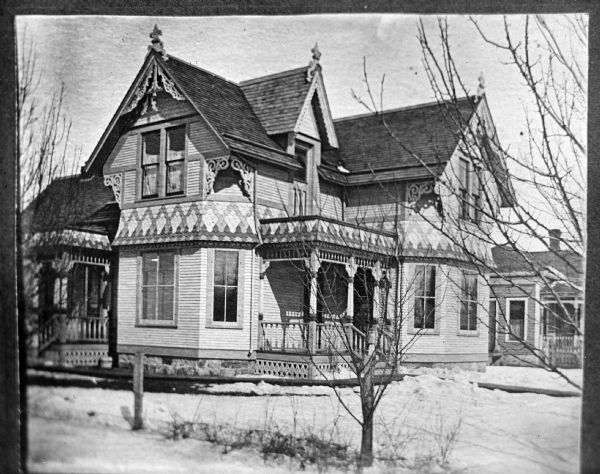 Copy photograph of an exterior view of a wooden house. The yard is covered in snow.