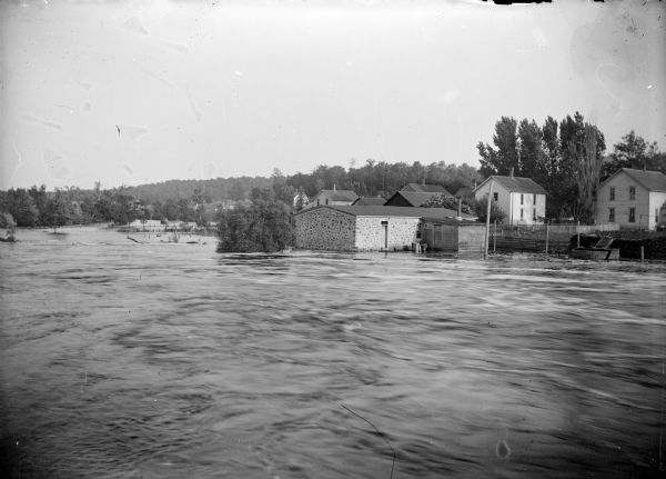 View across river of buildings along the river's edge. Identified as probably Melrose or Northbend, not Black River Falls. Probably from the flood of 1911.