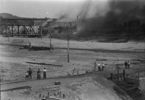 Elevated view of the fire at the McGillivray factory. Onlookers are standing in the road in the foreground.