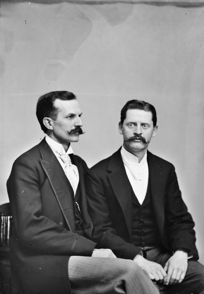 Waist-up studio portrait of two European American men, both with moustaches, posing sitting. The man on the left is identified as possibly Charles J. Van Schaick.
