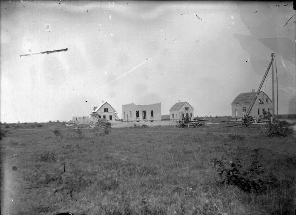 Exterior view of several wooden buildings under construction in a field. Identified as Vandrieul, Wisconsin.