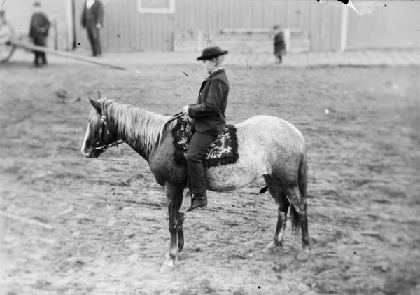 Boy sitting on a pony on a saddle possibly made of cloth.