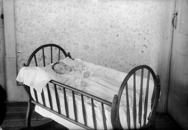 Indoor portrait of an infant post mortem, lying in a bassinet.
