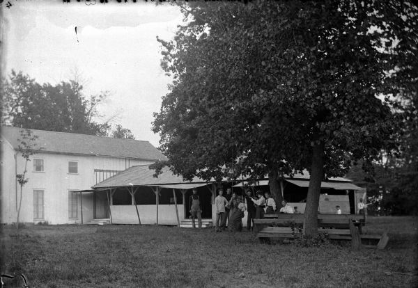 View across yard towards a group of people gathered under a tree. Identified as Tuttle's Cranberries, northeast of Mather.