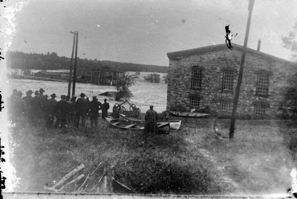 Exterior view of Black River Falls at the beginning of the flood of 1911. Note the roof of the powerhouse in the water, and the Spaulding wagon shop on the right about to go into the water.