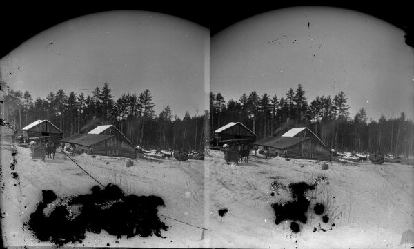 Exterior stereograph view across snow-covered field towards buildings and trees. Identified possibly as the York Iron Mine. *It looks like a logging camp.