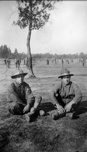 Copy photograph of an exterior view of two men in military uniform posing sitting on the ground. Identified as William and George Taylor at Camp Douglas.