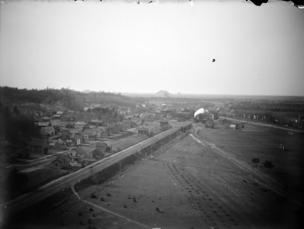 Exterior view identified as Camp Douglas from the south looking north. 
Elevated view of a town with a railroad track and an oncoming train in the center of the image.