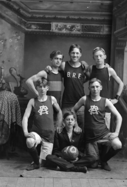 Studio portrait in front of a painted backdrop of six boys posing standing, kneeling, and sitting. Identified as BRF High School basketball team. The boys identified in the back row, left to right, ? Malchow, Alex Gunderson, and Neil Johnson. Front row, left to right, Price Howard, Howard Halverson, and Clarence Sprester.