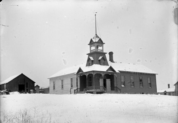 View across snow-covered ground towards a school or church building with a bell tower.