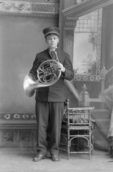 Studio portrait of a European American man posing standing and holding a french horn.