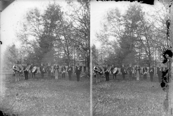 Outdoor group portrait, in stereographic form, of a musical band standing in a field in front of trees. Identified as possibly the Alma Center band.