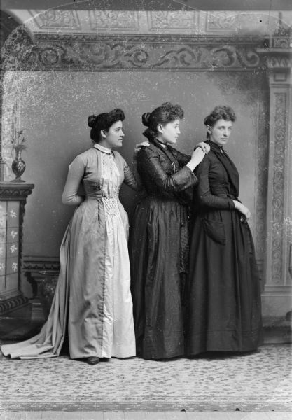 Studio portrait in front of a painted backdrop of three unidentified women posing standing.