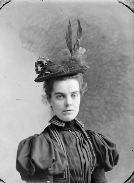 Quarter-length studio portrait of a European American woman posing sitting. She is wearing a dark-colored dress with puffed sleeves, and a hat with feathers and other decorations. The woman is identified as Cepba Cole, the daughter of Dr. Cole. She reportedly died in 1892.