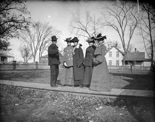 Outdoor portrait of a European American man and four European American women standing on a wooden walkway in a yard. Identified from left to right as: Jim Kinley, an unidentified woman, Lizzie Caries (the wife of Kinley), then the first wife of Henry Berg, and an unidentified woman. Location identified as probably the yard of the home of William Caries on German Hill before the 1911 flood. The house burned down just before the flood.