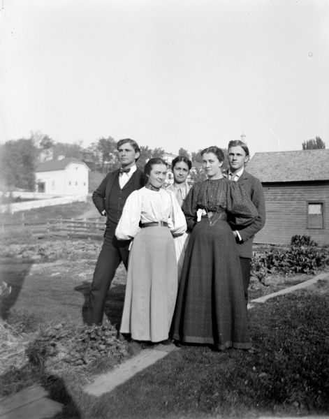 Outdoor portrait of three European American women and two European American men posing standing in front of several buildings in the distance. The women are identified as the daughters of Henry Steihl.