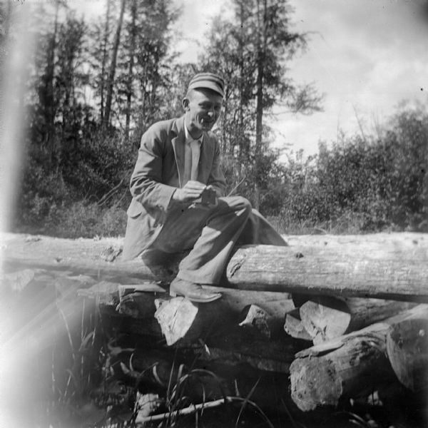 Outdoor portrait of an unidentified European American man posing sitting on logs, smoking a cigarette.