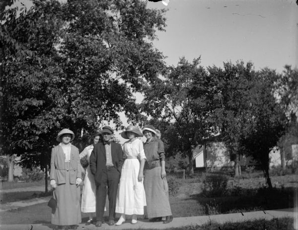 Outdoor group portrait of an unidentified group of people. Four women and one man are posing standing on a wooden walkway in a yard.
