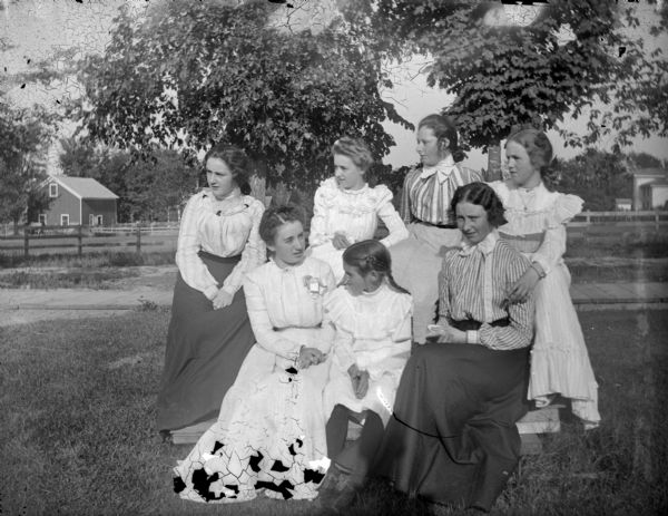 Outdoor group portrait of six unidentified women and a girl posing sitting and standing in a yard.