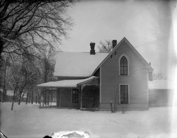 View across snowy yard towards a wooden house with a wrap-around porch.