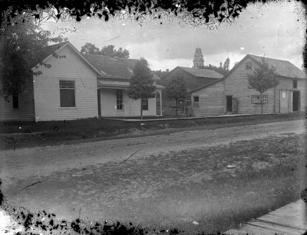 View from across street of two wooden houses. The house on the left is identified as the residence of Commodore Mason, William Peterson, and Mose Pauquette at about 214 Main Street. The building on the right is probably a stable.