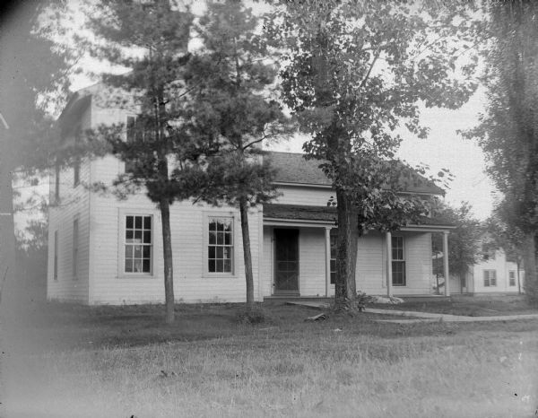 View across lawn towards a house with several medium sized trees in front. The house is identified as the Robert P. Rainey residence at the southeast corner of North Fifth and Pierce Streets.