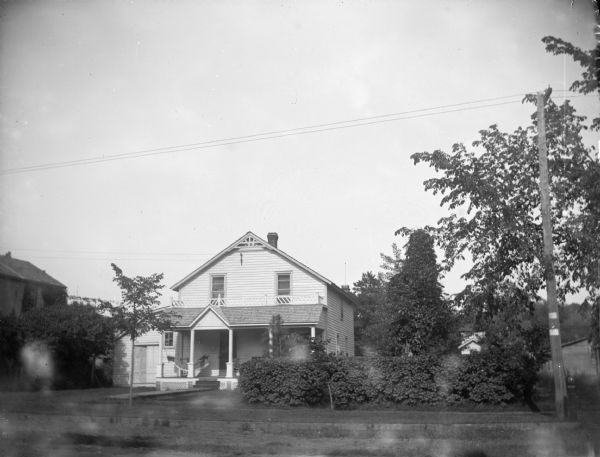 Exterior portrait of a two-story wooden house with large lilac bushes on the right side. House identified as the residence of J. Ogden at 213 North Fifth Street.
