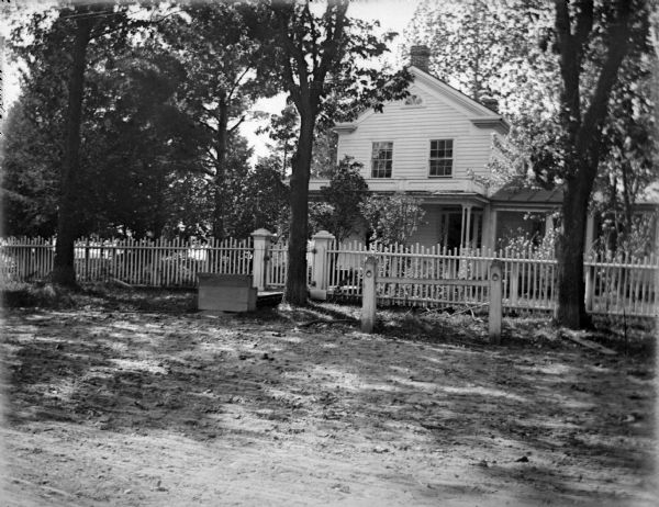 Exterior portrait of a two-story wooden house surrounded by a picket fence and trees. House identified as the residence of C. C. Pope on the northwest corner of Main and Sixth Streets.