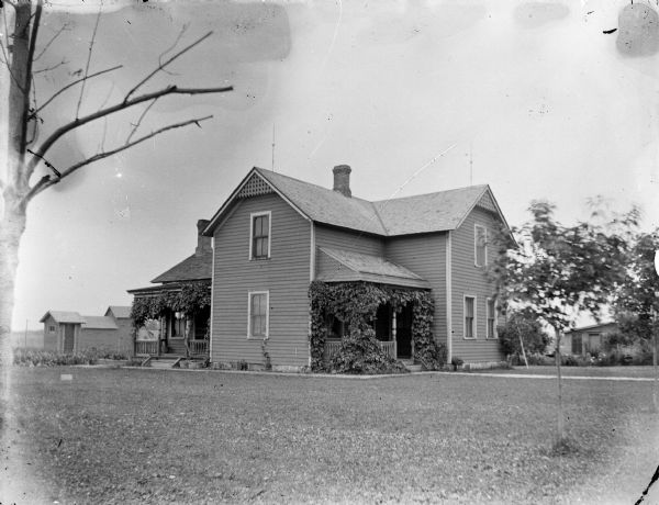 Exterior portrait of a two-story wooden house with two porches with hanging vines.