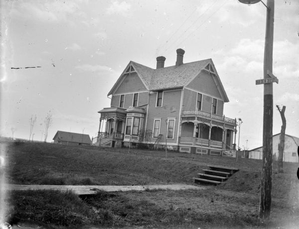 Outdoor view across lawn towars a two-story wooden house with two chimneys and two porch entrances at the corner of Beech Street and Huron Street. There is a set of stairs in the foreground.