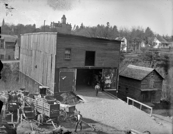Elevated view of a two-story wooden barn, with trees and a school building in the background. The barn is identified as the barn for the Freeman Hotel, behind Jones L. & M. on Harrison Street.