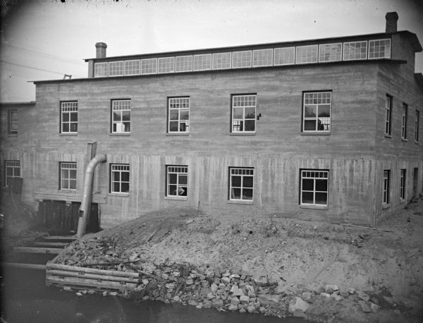 Outdoor view of a two-story wooden building, probably the McGillivray factory built about 1913 across the bridge at Water and Harrison Streets.