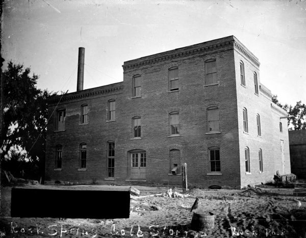 Outdoor view of a three-story brick building with a smokestack. Writing on the negative reads: "Rock Spring Cold Storage, Rock, Rock." Identified as Rock Spring Cold Storage, reportedly the original Oderbolz Brewery, southeast corner of Pierce and South Fourth Streets.