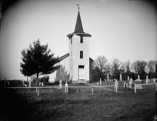 Outdoor view of a church surrounded by several grave markers. Identified as the Little Norway Lutheran Church.