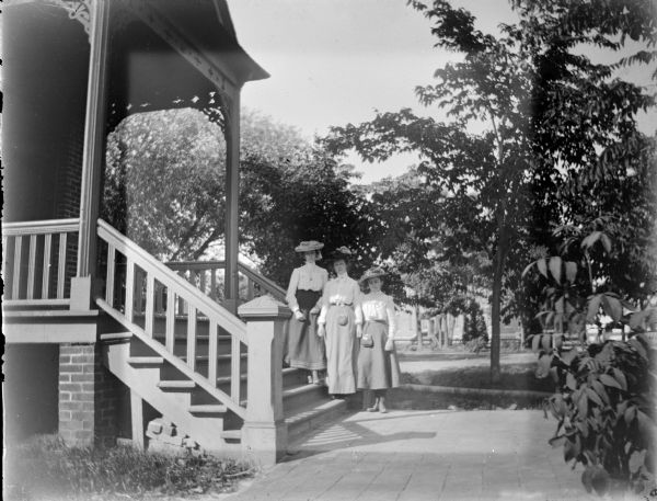 Outdoor group portrait of three European American women posing standing on the stairs of a building. Location identified as the Methodist Church.