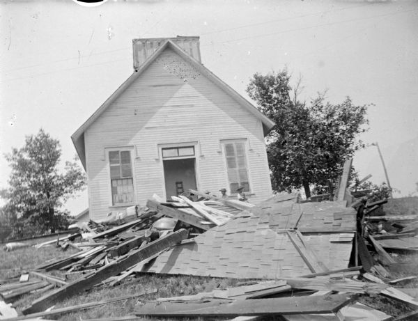 View towards the front of a church, with wooden debris in the forground. People are standing near the entrance behind the debris. Identified as the old Catholic Church (formerly a Universalist Reformed) located on the Main Street hill, whose steeple reportedly blew off in 1900.