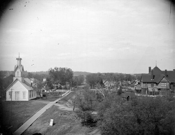Elevated view of town, with a church on the left and houses on the right. Identified as taken from the Jackson County Courthouse, with the church on the left identified as originally an Universalist Church built in 1869, then a German Reform Church, and finally a Catholic Church, torn down in 1941 or 1943.