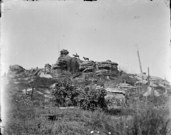 Outdoor view looking up a hill towards a man posing sitting on horse on top of a rock formation. Identified as the east end of Bruce Mound.