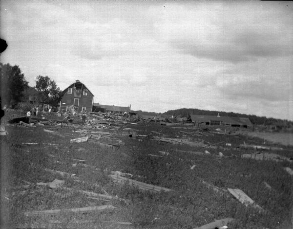 Outdoor view across field towards a wooden structure in a field full of damage debris. Probably the aftermath of a tornado.