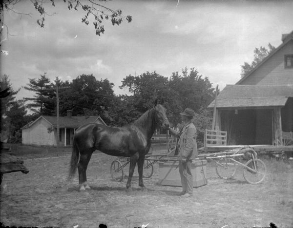 Outdoor view of a man displaying a single horse in front of several wooden buildings in town.