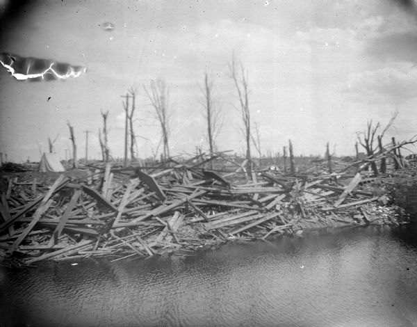 Exterior portrait of wooden debris near a water's edge and a canvas tent.
